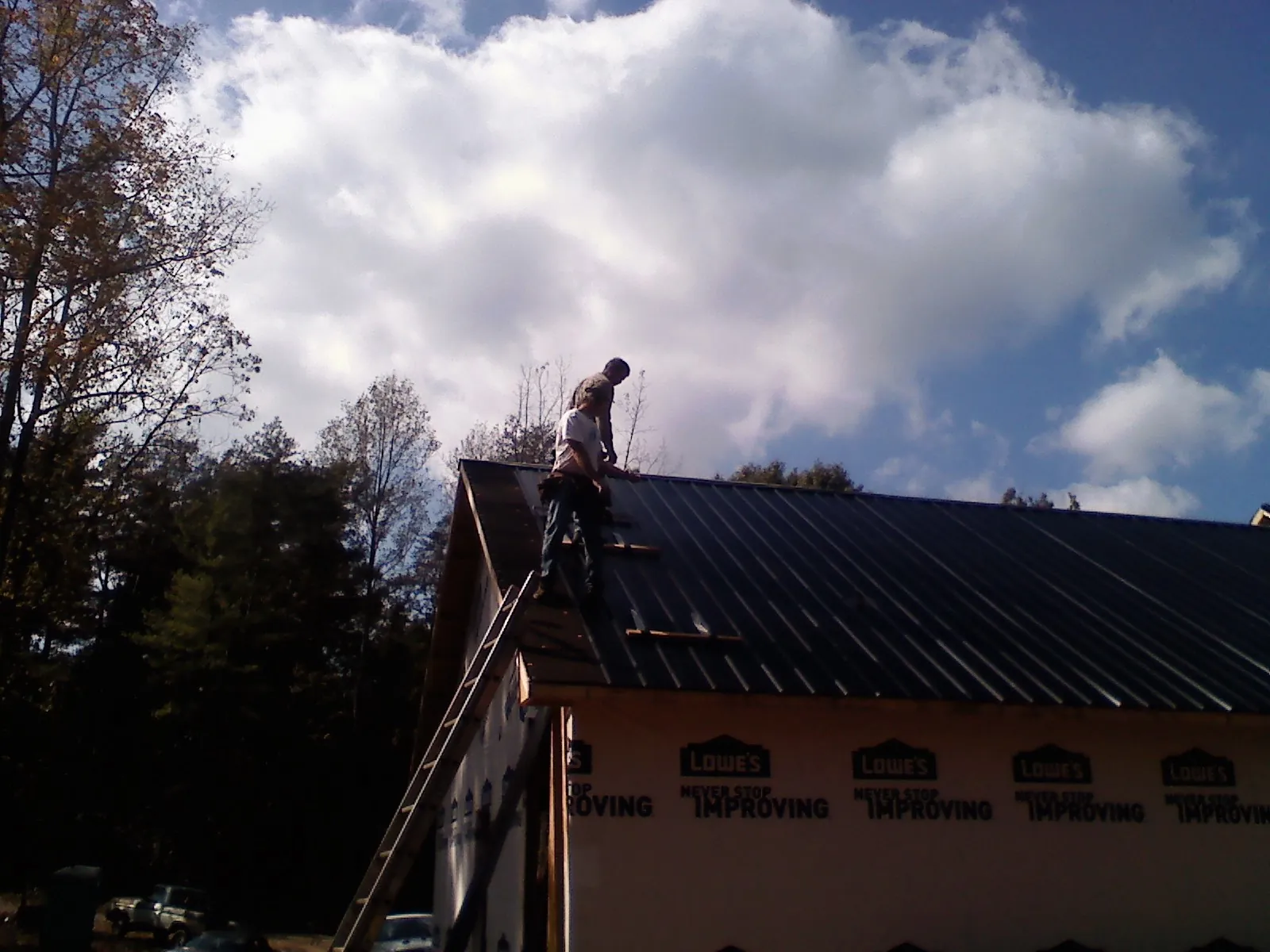 Roofer fastening dark metal panels high against a cloudy sky, from a Roof Inspection job in Glenwood